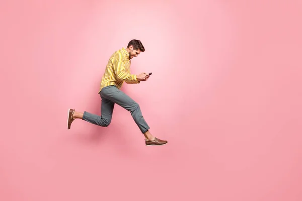 Full length profile photo of beautiful guy jumping high holding phone rushing on romantic date wear hipster ριγέ πουκάμισο παντελόνι απομονωμένο ροζ χρώμα φόντο — Φωτογραφία Αρχείου