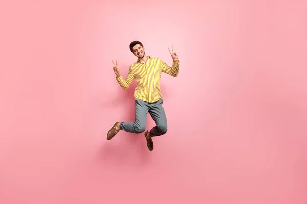 Foto de longitud completa de chico guapo saltando alto disfrutar de la hora de verano mostrando símbolos v-signo de usar pantalones de camisa de rayas hipster aislado de color rosa fondo —  Fotos de Stock