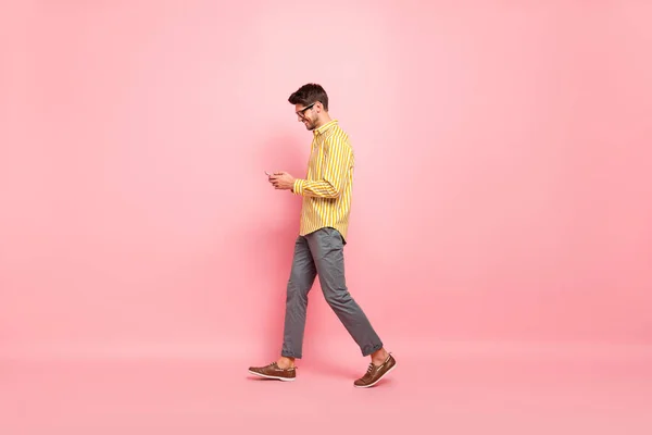 Full size profiel foto van knappe man gaan straat afgewerkt werkweek typen vriendin sms telefoon slijtage specs gestreepte shirt broek geïsoleerde roze kleur achtergrond — Stockfoto