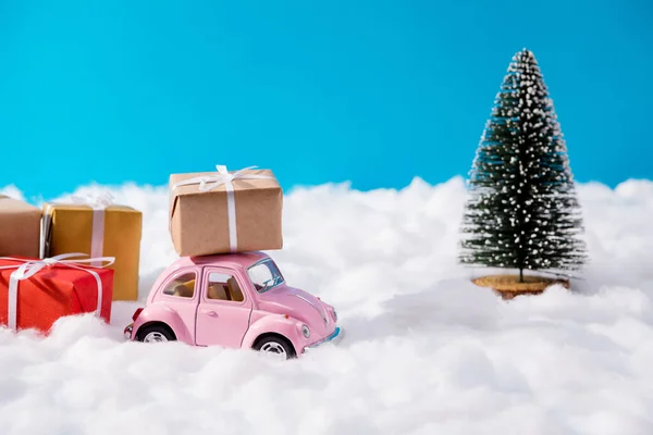 Різдвяний розпродаж. Крупним планом фото з маленьким ретро-рожевим автомобілем в оточенні багатьох великих подарункових коробок біля вічнозеленого банера соснового дерева для новорічної реклами барвистий орнаментний фон — стокове фото
