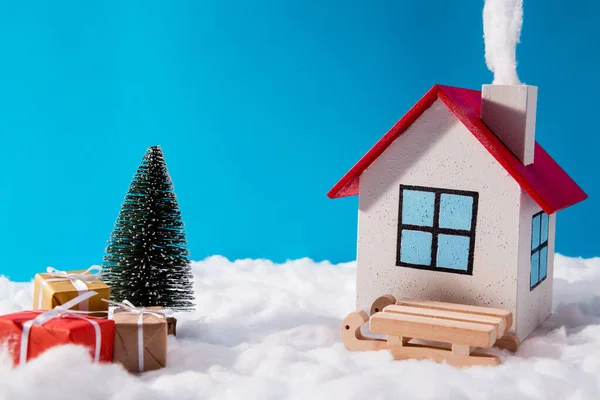 Kleines Spielzeug Weihnachtsmann bequemes Haus steht auf Nordpol mit rotbraunen Geschenkboxen Holzschlitten Tanne unter blauem Himmel Hintergrund — Stockfoto
