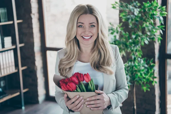 Fénykép gyönyörű szőke üzletasszony jött a munkahelyen reggel kezében friss tulipán csokor karját boldog férj meglepetés modern kényelmes iroda — Stock Fotó