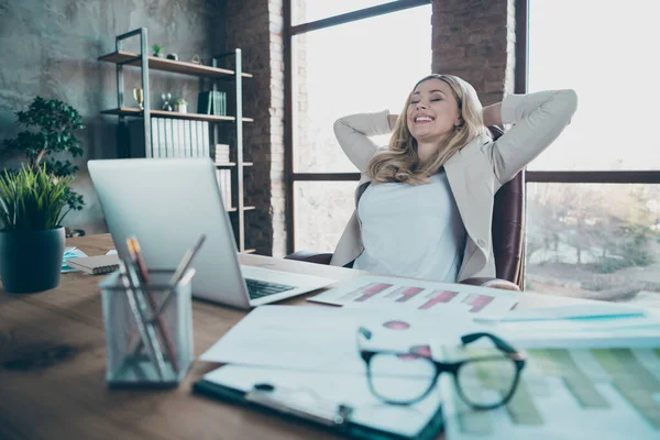 Foto de la hermosa mesa de cuaderno de señora rubia de negocios cogida de la mano detrás de la cabeza con los ojos de pausa cerrada silla de estar satisfecha chaqueta formalwear en la oficina moderna —  Fotos de Stock