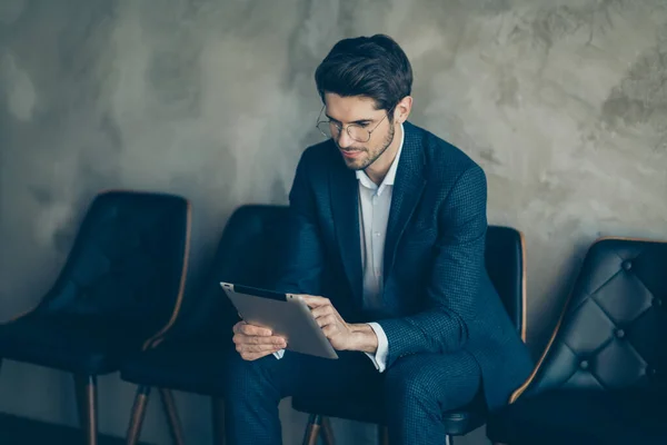 Retrato de agente enfocado trabajo representativo de negocios en su tableta sentarse en la silla esperar a reunirse con sus socios clientes usan pantalones de chaqueta con estilo azul aislado sobre fondo de color gris — Foto de Stock