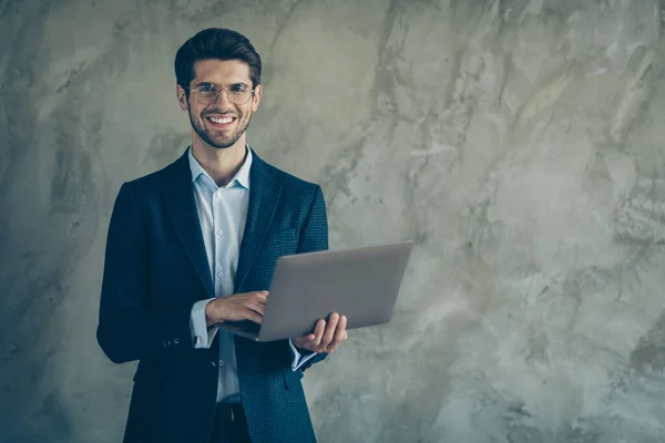 Фото веселого позитивного зубастого сияющего человека, держащего ноутбук с улыбкой на руках рядом с пустым пространством, просматривающего изолированный серый цвет фона — стоковое фото
