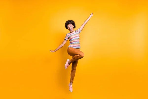 Full length body size photo of cheerful positive funky ecstatic overjoyed girl in orange pants striped t-shirt footwear jumping isolated vibrant color background