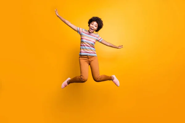 Longitud completa tamaño del cuerpo foto de alegre joven bastante niña con las manos como la propagación de alas pantalones anaranjados rayas camiseta rizado ondulado aislado color vivo fondo —  Fotos de Stock