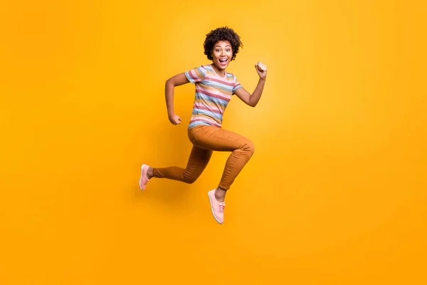 Foto profil tubuh penuh melompat tinggi kulit gelap bergelombang wanita balap kecepatan juara berlari mengenakan pakaian musim panas yang kasual terisolasi latar belakang warna kuning cerah — Stok Foto