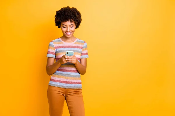 Portret pozytywnej wesołej dziewczyny ciemnej skóry korzystać z jej smartfona czytać wiadomości w mediach społecznościowych blogowanie nosić stylowy letni strój odizolowany na tle koloru połysk — Zdjęcie stockowe