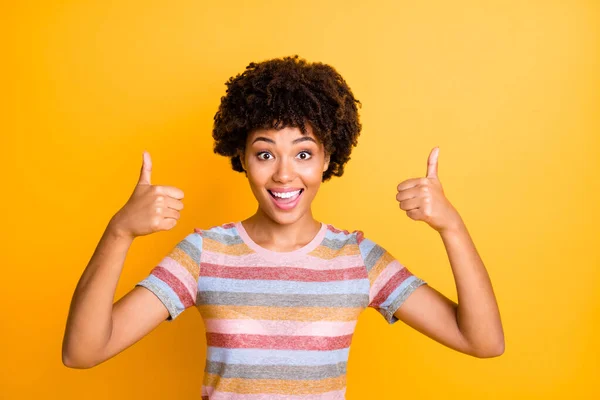 Photo of beautiful dark skin lady holding thumbs raised air expressing agreement and positive attitude wear casual striped t-shirt isolated yellow background — ストック写真