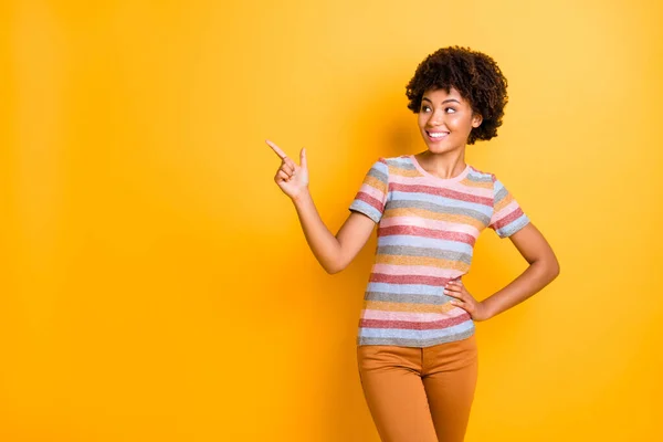 Photo of cheerful positive cute nice charming pretty girl pointing at empty space where your ads should be wearing striped t-shirt pants trousers isolated over yellow vivid color background — Stock Photo, Image