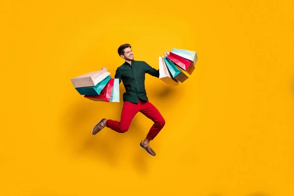 Longitud completa tamaño del cuerpo foto de alegre positivo guapo hombre saltando sosteniendo numerosos paquetes que regresan del centro comercial aislado color vivo fondo — Foto de Stock