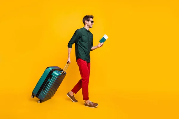 Tam boy vücut boy yan plan fotoğrafı. Elinde pasaportu ve uçağa binmek için biletleri olan bir adam. Kırmızı pantolonlu, izole edilmiş sarı arka planlı bir uçağa doğru yürüyor. — Stok fotoğraf