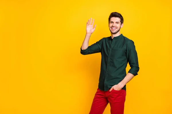 Foto de alegre positivo cabelos castanhos confiante cara segurando mão no bolso de calças vermelhas sorrindo toothily acenando com a mão em você isolado cor vibrante fundo — Fotografia de Stock