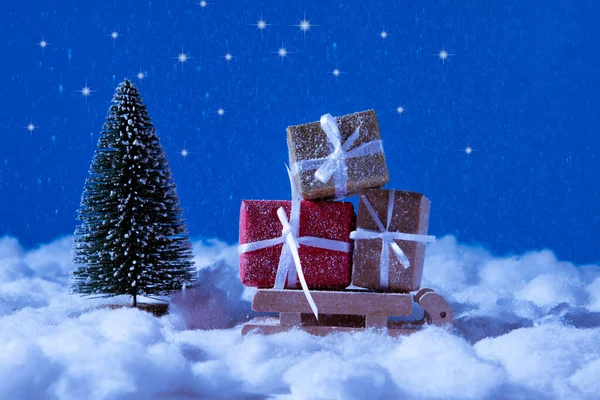 Foto av små leksak Santa claus slädar bär gula röda bruna presentaskar bråttom för jul tid firande stå nära gran träd under natten blå himmel bakgrund — Stockfoto