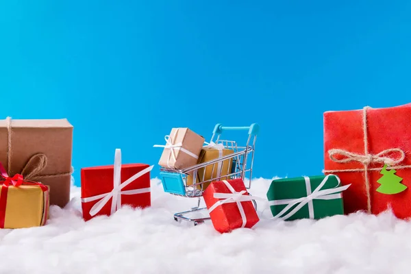 Muchas x-mas pequeñas cajas de regalo marrones amarillas rojas verdes se quedan dentro del carrito del supermercado x-mas time Christmas season shopping concept stand under blue sky background — Foto de Stock