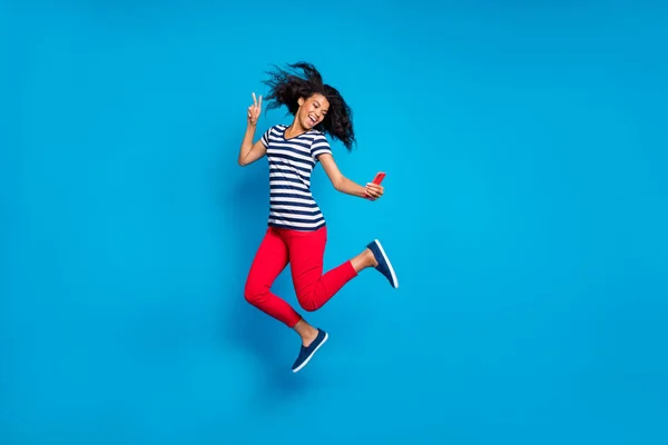 Vände full längd kroppsstorlek foto av glada positiva glada galen flicka filma sig själv med selfie bär byxor röd randig t-shirt hoppa isolerad levande färg blå bakgrund — Stockfoto