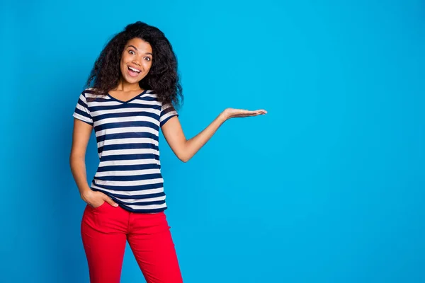 Photo of cheerful positive nice pretty cute attractive girlfriend holding hand in pocket holding empty space smiling toothily in striped t-shirt isolated over vivid blue color background — Stock Photo, Image