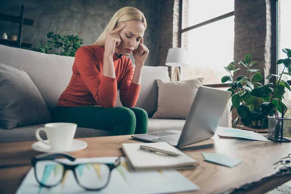 Foto av blond företag dam trött hårt arbetande hålla tempel lider fruktansvärd migrän bära specs orange pullover sitter soffa bord anteckningsbok dagbok kaffe inomhus — Stockfoto