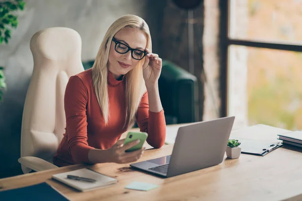 Charmante Chefin mit orangefarbenem Rollkragen sitzt Tisch erhalten Social-Media-Benachrichtigung lesen SMS von Kunden im Büro tragen roten Rollkragen — Stockfoto