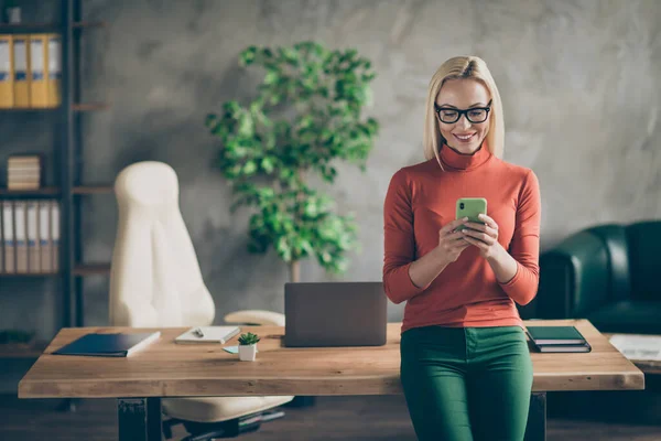 Retrato de la mujer propietaria de la empresa inteligente usar el teléfono inteligente charlando con los empleados colegas de pie cerca de la mesa de madera en el loft de la oficina usar cuello alto rojo —  Fotos de Stock