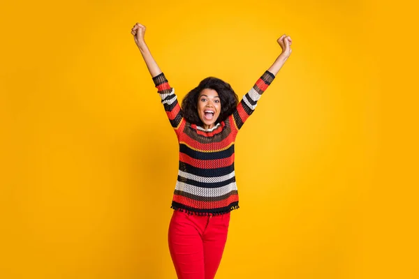 Retrato de emocionado loco afro chica americana se siente regocijo funky escuchar noticias maravillosas levantar los puños gritar wow omg desgaste casual estilo suéter pantalones rojos aislados sobre color amarillo — Foto de Stock