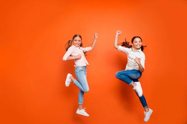 Foto de longitud completa de dos amigas rubias de cabello castaño positivas con colas largas saltar levantar los puños sentir contenido desgaste traje casual aislado sobre fondo de color naranja — Foto de Stock