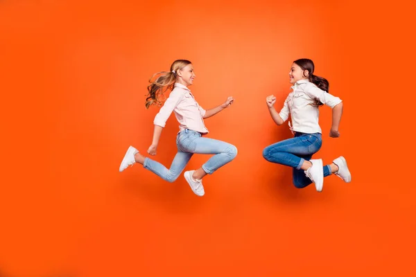 Полноразмерная фотография профиля с позитивными забавными двумя малышами, расслабляющими отдых прыжком в белую рубашку джинсы и джинсы на оранжевом фоне — стоковое фото
