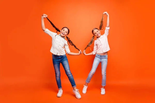 Foto in voller Größe von funky lustige zwei Kinder Mädchen entspannen Freizeit Herbstferien halten Pferdeschwänze genießen Wochenenden tragen lässige Jeanskleidung isoliert orange Farbhintergrund — Stockfoto