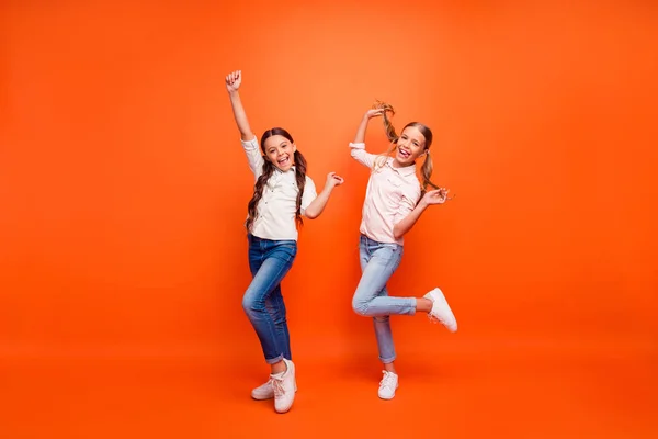 Full kropp foto av funky galen två flickvänner har kul på hösten helger höja händerna nävar hålla armar flätor bära vit skjorta sneakers isolerad orange färg bakgrund — Stockfoto