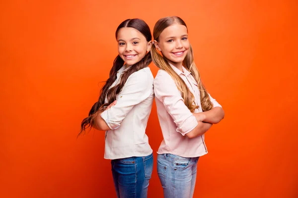 Retrato de equipo alegre positivo de dos niñas lindas de pie back-to-back listo resolver las soluciones de la escuela decidir las decisiones de desgaste traje moderno aislado fondo de color naranja —  Fotos de Stock