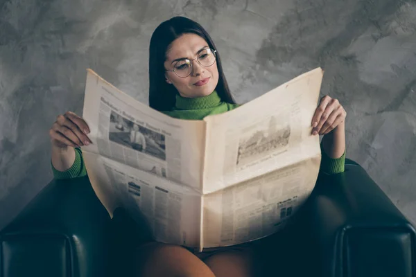 자신감 있게 안락 의자에 앉아 신문의 헤드라인을 읽고 있는 진지 한 여성의 사진 고립 회색 벽 콘크리트 배경 — 스톡 사진
