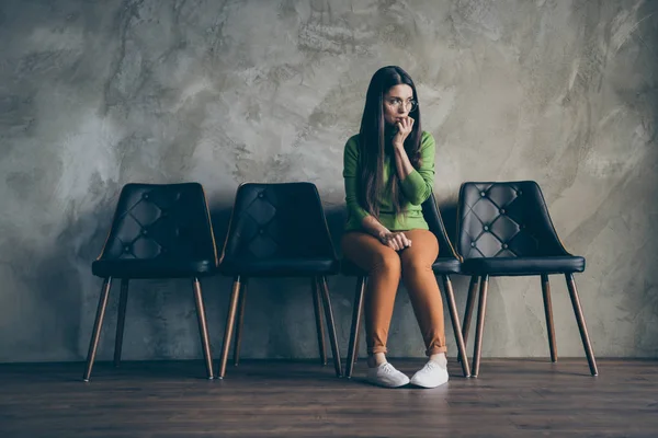 Volledige lengte body size foto van nerveuze vrouw zitten in stoel naast lege ruimte degenen in oranje broek schoenen geïsoleerde grijze muur beton kleur achtergrond — Stockfoto