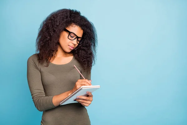 Portrait de concentrée mulâtre fille écrire dans copybook préparer projet porter lunettes chemise moderne isolé sur fond de couleur bleue — Photo