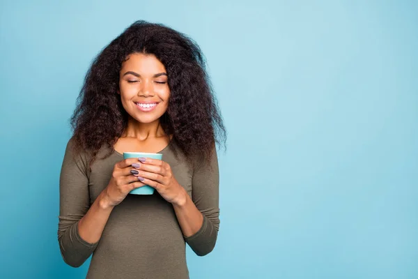 Portret pozytywnej wesołej afro amerykańskiej dziewczyny trzymać kubek z gorącą kawą cieszyć zapach czuć spokój spokojny w weekendy wolny czas nosić casual styl skoczek izolowany na niebieskim tle koloru — Zdjęcie stockowe