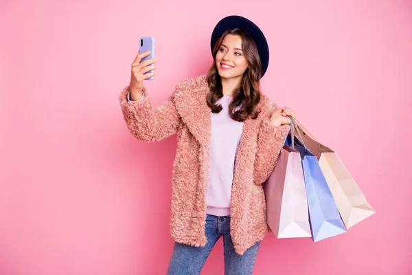 Φωτογραφία από την όμορφη κυρία μοντέλο χιλιετή πολλά πακέτα τηλέφωνο κάνοντας selfies για τα ταξίδια blog εμπορικό κέντρο φορούν κομψό χειμώνα χνουδωτό σακάκι ρετρό τζιν καπέλο απομονωμένο ροζ φόντο — Φωτογραφία Αρχείου