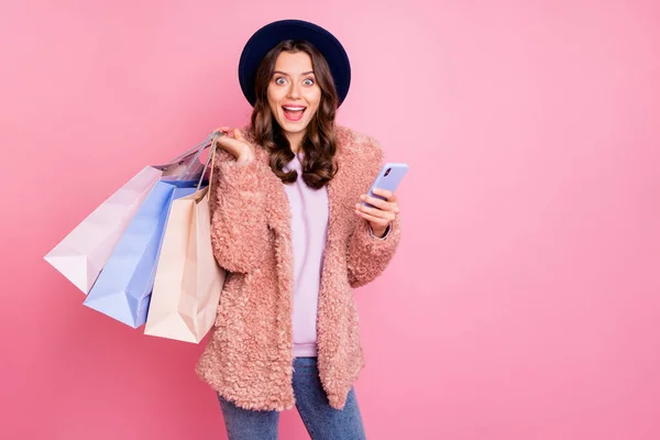 Photo of beautiful millennial model lady tourist hold many packs telephone reading good comments mall wear stylish fluffy jacket retro blue hat jeans isolated pink background — Φωτογραφία Αρχείου