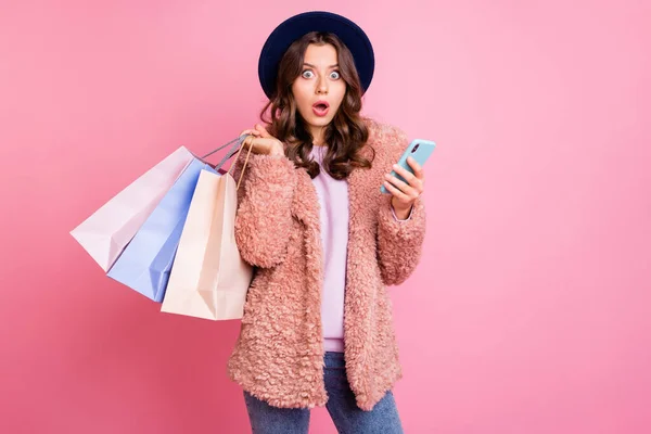 Photo of pretty millennial lady hold many packs telephone reading unexpected negative comments wear stylish fluffy jacket trendy retro blue hat isolated pink background — ストック写真