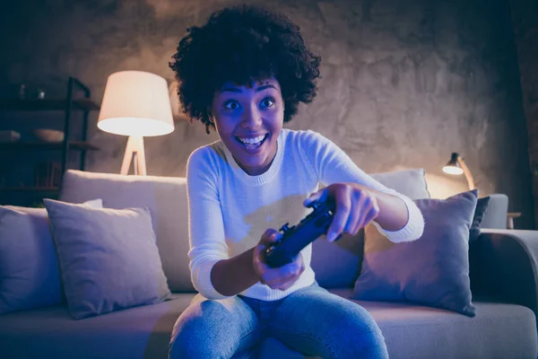 Portret van vrolijke funky afro amerikaanse meisje houden joystick spelen video game genieten plezier zitten divan in appartement kamer huis binnen — Stockfoto
