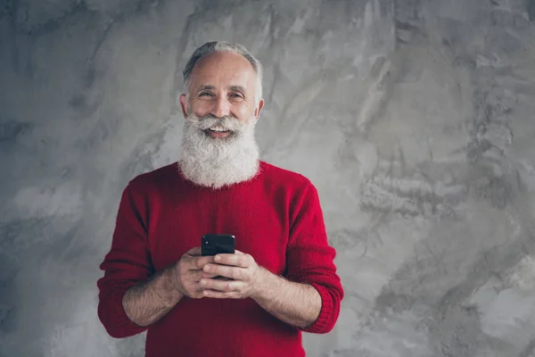 Портрет праздничный современный белый волосы старик блоггер использовать смартфон наслаждаться Рождество скидки типа текст поздравления носить красный пуловер изолированы серый бетонный фон стены цвета — стоковое фото
