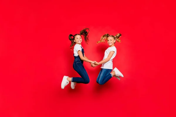 フルサイズのプロフィール側の写真の2人の小さな人々かわいい子供たちの女の子が持っているx-mas休日ジャンプホールド手を感じる夢夢のような着用カジュアルな白いtシャツ隔離された赤い色の背景 — ストック写真