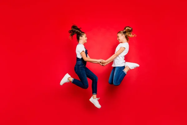 Los mejores amigos para siempre. Lado de perfil de longitud completa de dos divertidos niños divertidos salto de vacaciones de primavera disfrutar de usar camisetas blancas jeans zapatillas de deporte monos aislados de color rojo de fondo — Foto de Stock