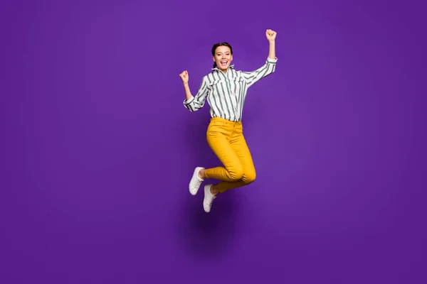 ¿Sí? Foto de longitud completa de la señora bonita loca saltando alto celebrando la victoria levantando puños deportes ventilador usar camisa rayada pantalones amarillos aislados color púrpura fondo —  Fotos de Stock