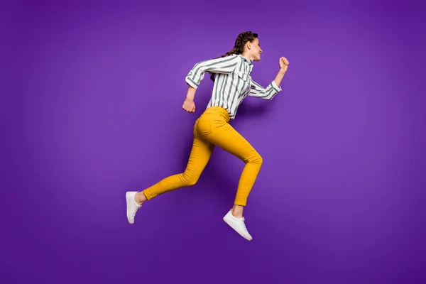 Teljes test profil fotó csinos hölgy jumping magas rohanó kedvezmény eladási árak vásárlás kopás csíkos ing sárga nadrág elszigetelt lila szín háttér — Stock Fotó