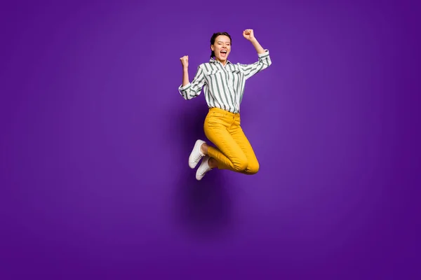 Teljes méretű fotó őrült csinos hölgy jumping magas versenyképes sportnő ünneplő győzelem emelése öklöt visel csíkos ing sárga nadrág elszigetelt lila színű háttér — Stock Fotó