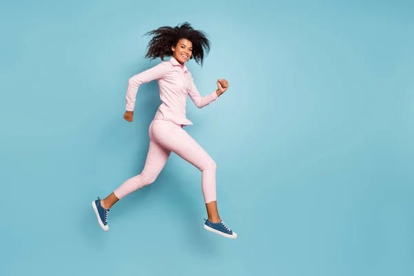 Full length photo of amazing dark skin wavy lady jumping high speed racing participator wear pink πουκάμισο παντελόνι απομονωμένο μπλε χρώμα φόντο — Φωτογραφία Αρχείου