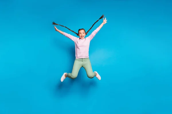 Full length photo of pretty crazy lady long braids flying jumping high rejoicing free time carefree mood wear casual pink pullover green pants isolated blue color background