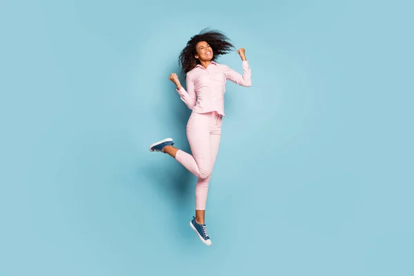 フル長さの写真の驚くべき暗い肌の女性ジャンプ高い祝うクールな勝利勝利勝利ピンクのシャツのズボンのスニーカー隔離された青の色の背景 — ストック写真