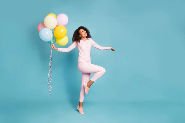 Volledige lengte foto van verbazingwekkende golvende donkere huid dame met veel lucht ballonnen opgewonden positieve partij stemming dragen roze shirt broek geïsoleerde blauwe kleur achtergrond — Stockfoto