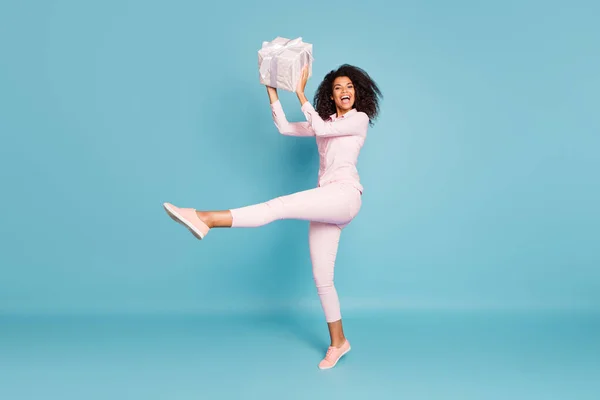 Full length photo of amazing wavy dark skin lady holding large wrapped giftbox came to party best guest wear pink shirt pants isolated blue color background